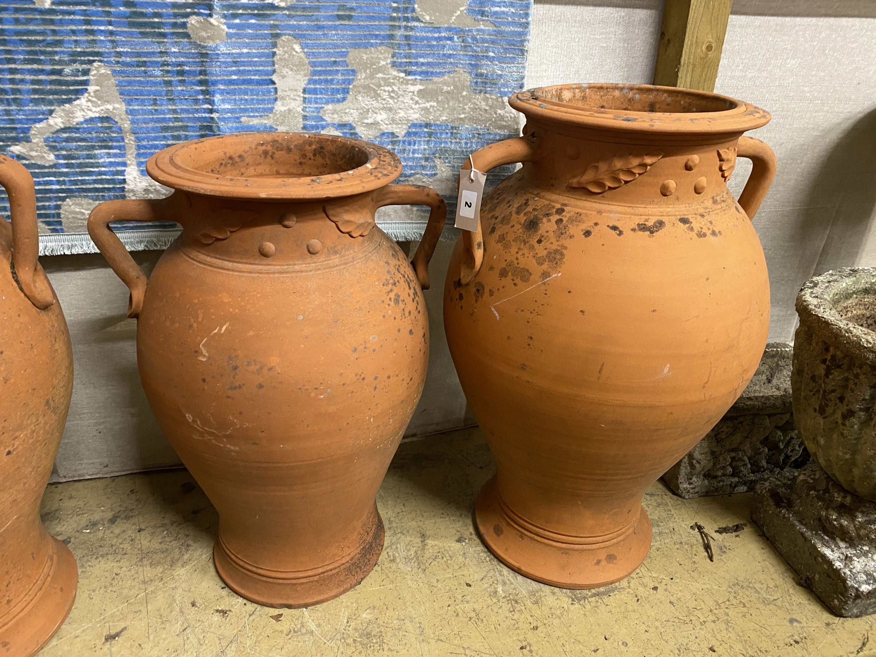 A set of three terracotta baluster garden urns moulded with leaves, largest height 72cm
